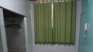 A small, private bathroom with a shower area, a bed with pillows, and a green curtain. - Hotel Avenida (Vitoria)