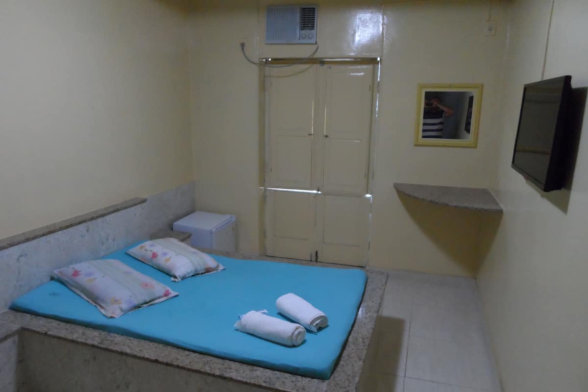 Una habitación pequeña y limpia con cama, una mesita, inodoro y zona de ducha.