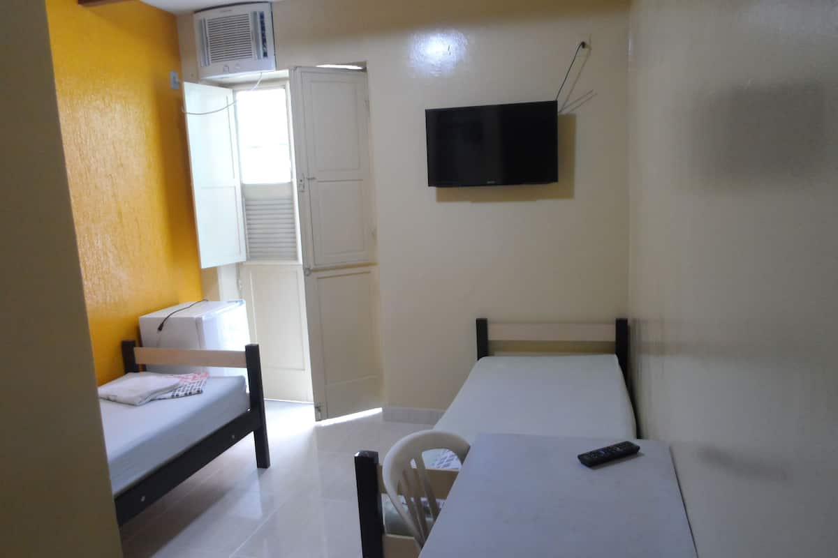 Una habitación pequeña y funcional con cama, escritorio y televisor.