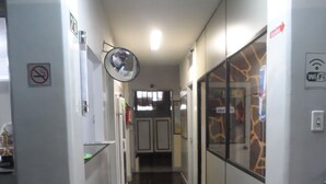 A narrow hallway with a wooden floor, white walls, and a glass door with a giraffe pattern. There are signs indicating no smoking and WiFi availability. - Hotel Avenida (Vitoria)