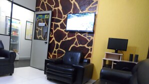 A room with a giraffe-patterned wall, a TV mounted on it, a sofa, a chair, and a small table with a lamp. - Hotel Avenida (Vitoria)