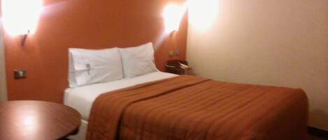 A hotel room with a bed, a round table, and two wall-mounted lights.