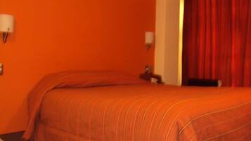 Habitación de hotel con dos camas, paredes anaranjadas y cortinas rojas.