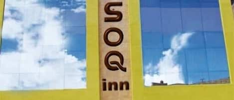 Un hôtel dont la façade est ornée d’un grand panneau indiquant « MOSQ », doté de larges fenêtres et d’une entrée symétrique avec une porte centrale.