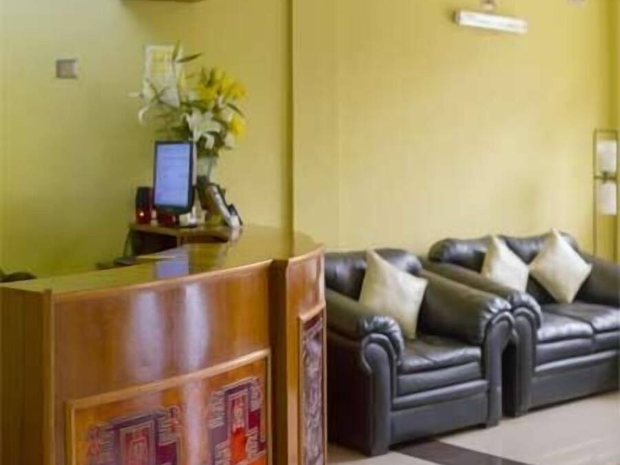 Un mostrador de recepción con un monitor de computadora, un jarrón con flores y un sofá de cuero negro con almohadones.