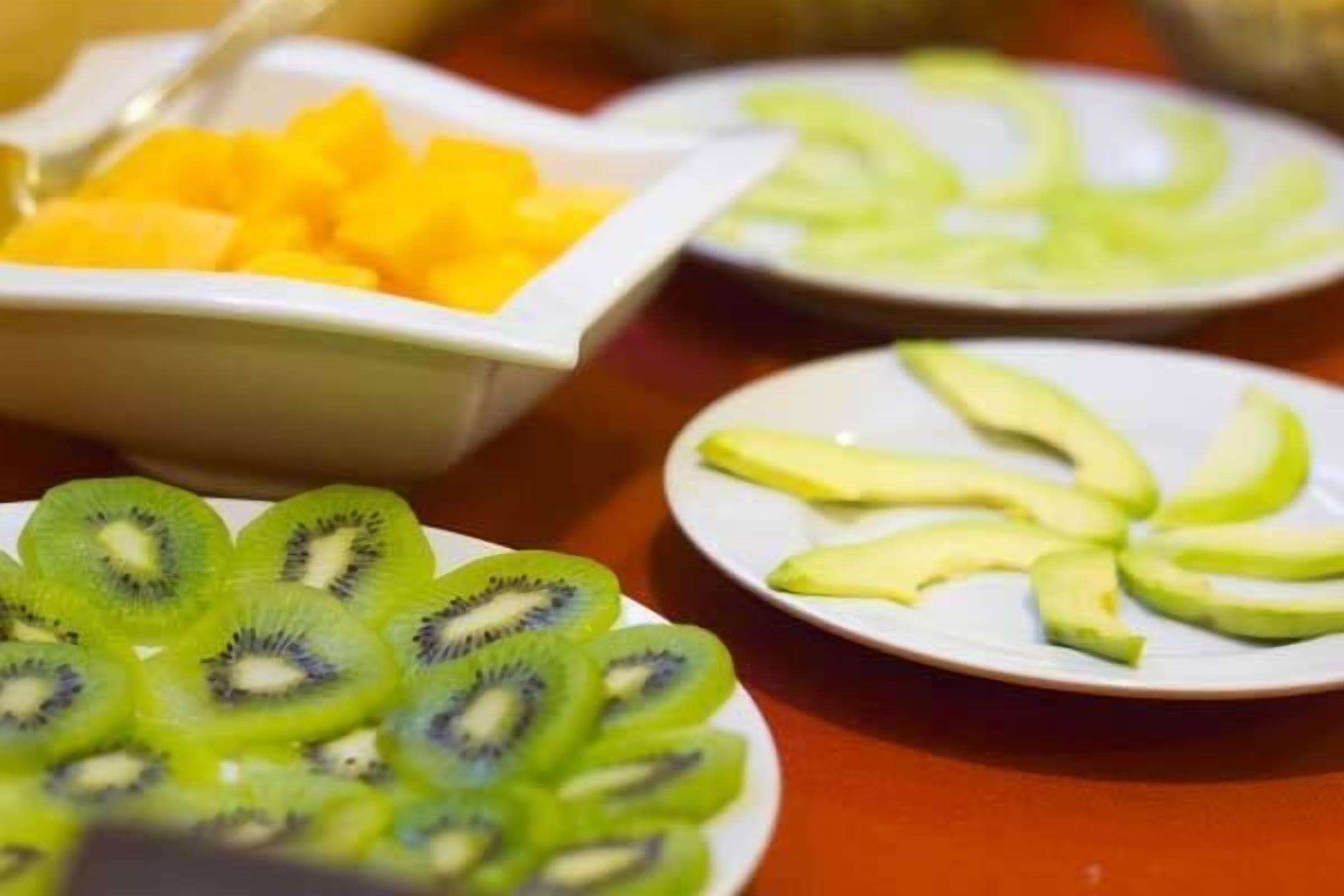 Une table avec des bols remplis de fruits coupés en tranches, notamment des kiwis, des mangues et des avocats.
