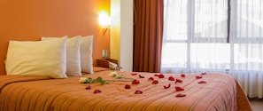 A hotel room with a bed, pillows, a nightstand, a lamp, and a window with curtains. - Mosoq Inn (Puno)