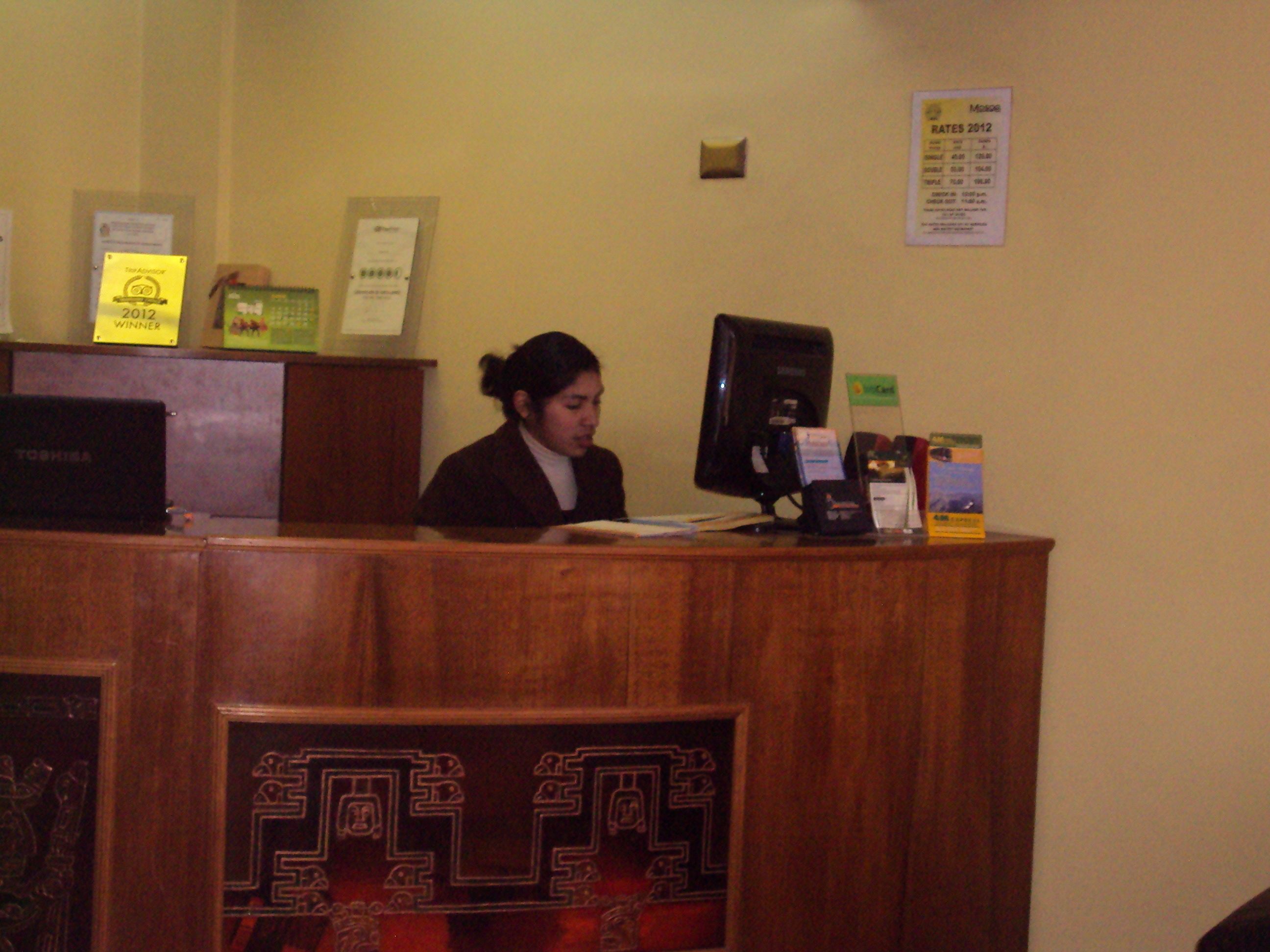 A reception desk with a computer, a monitor, and various items on it. There are signs on the wall, including one that says "Winner 2012".