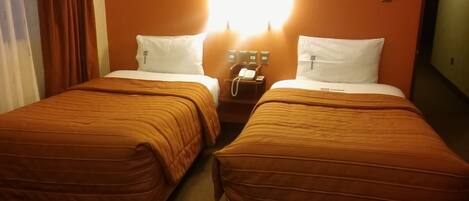 A hotel room with two beds, each with a brown bedspread and white pillows, and a nightstand with a telephone between them.