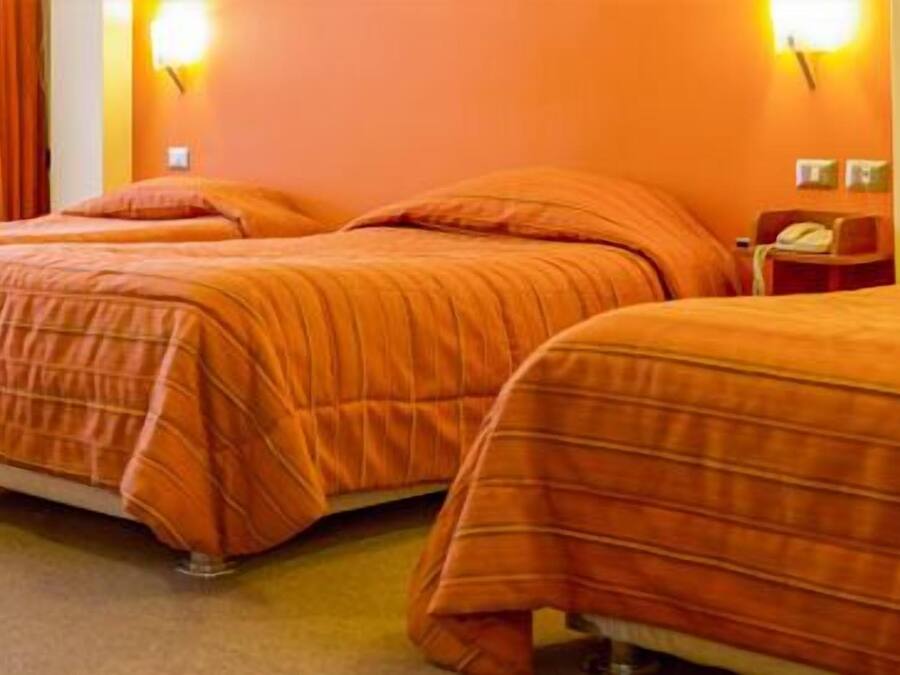 Una habitación de hotel con tres camas, cada una con ropa de cama naranja.