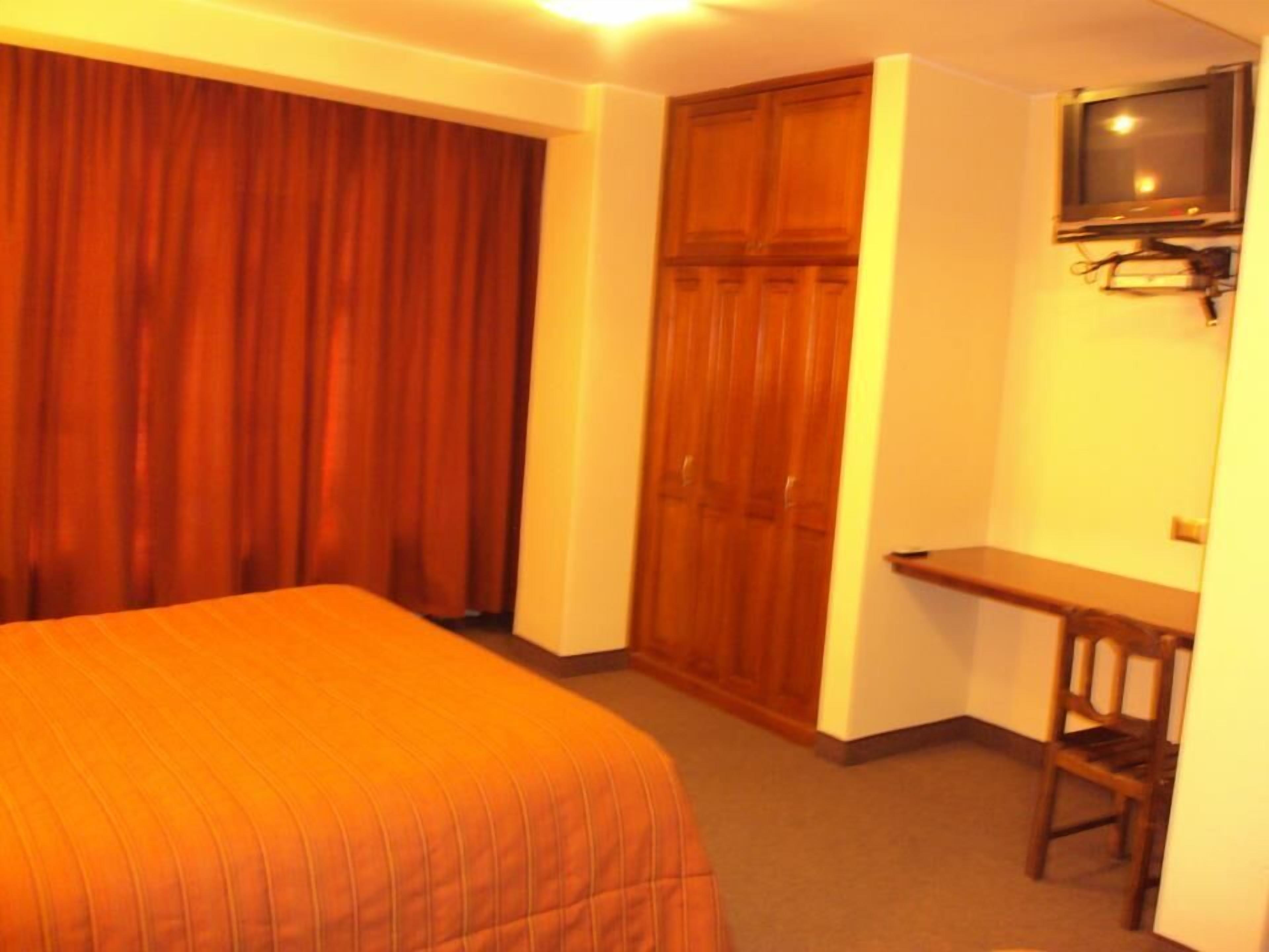 A hotel room with a bed, a desk, a chair, a television, and a wardrobe.
