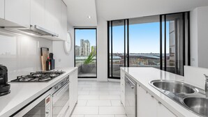 Eine moderne Küche mit weißen Schränken, einer Edelstahlspüle und Blick auf die Stadt durch große Fenster.