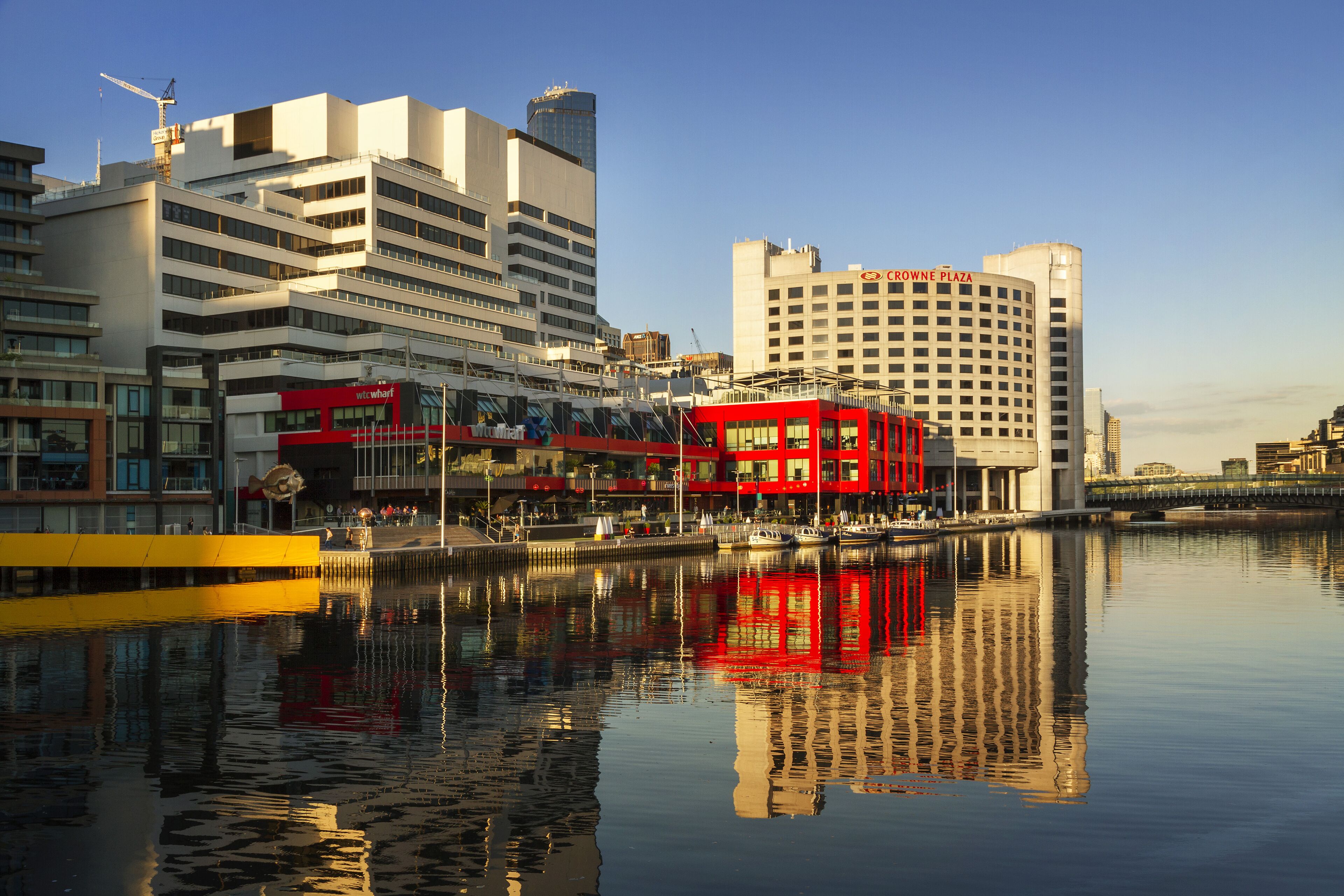 A waterfront hotel with a red facade, multiple floors, and a reflection in the water.