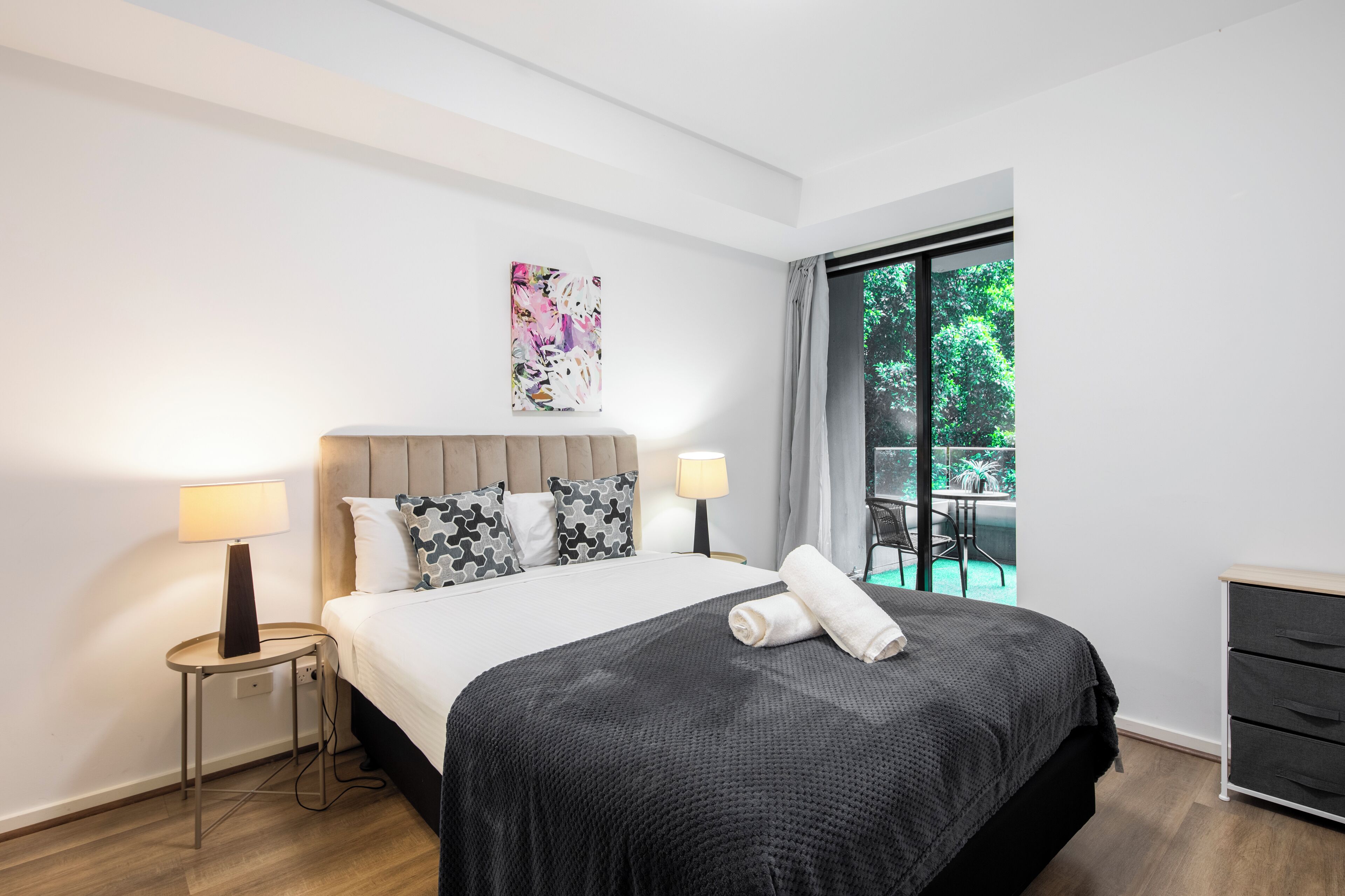 Habitación de hotel moderna con una cama grande, dos lámparas de noche, un cuadro y vistas al exterior.