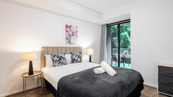 Habitación de hotel moderna con una cama grande, dos lámparas de noche, un cuadro y vistas al exterior.