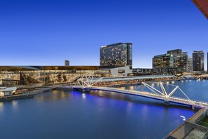 Un pont moderne enjambant une rivière paisible, entouré d’immeubles de grande hauteur dont les fenêtres sont illuminées.