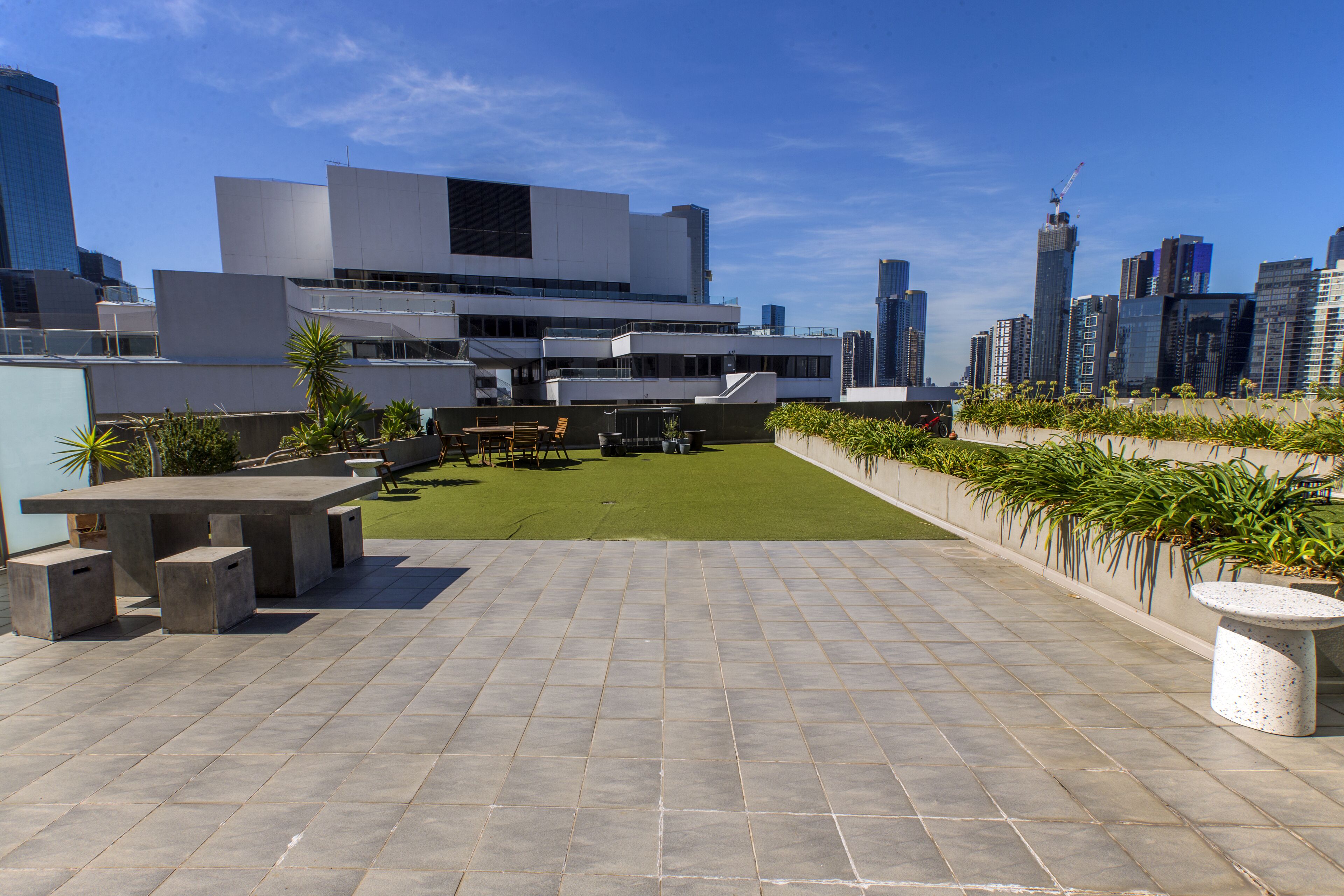 A rooftop terrace with a concrete table and benches, surrounded by a low wall with potted plants.