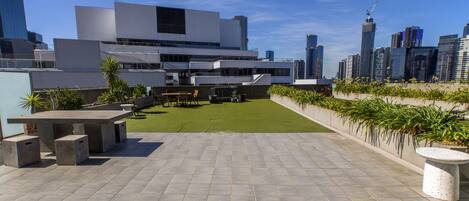 A rooftop terrace with a concrete table and benches, surrounded by a low wall with potted plants.