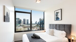 Ein modernes Hotelzimmer mit einem großen Bett, Blick auf die Stadt durch ein Fenster und einem gerahmten Bild an der Wand.