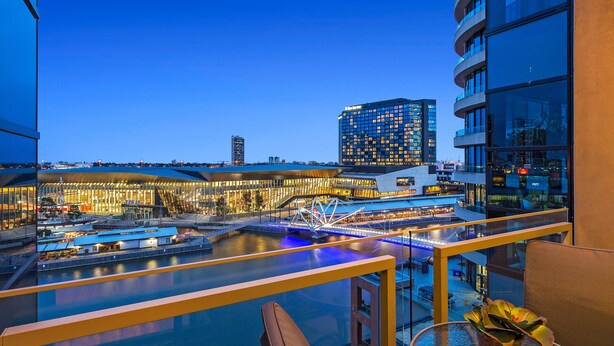Ein modernes Hotel mit Glasbalkon und Blick auf eine Uferpromenade, inklusive Pool und Brücke.