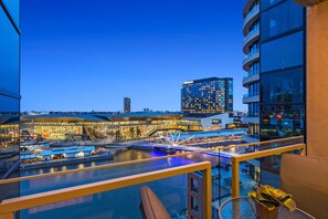 A modern hotel with a glass balcony overlooking a waterfront area, featuring a pool and a bridge.