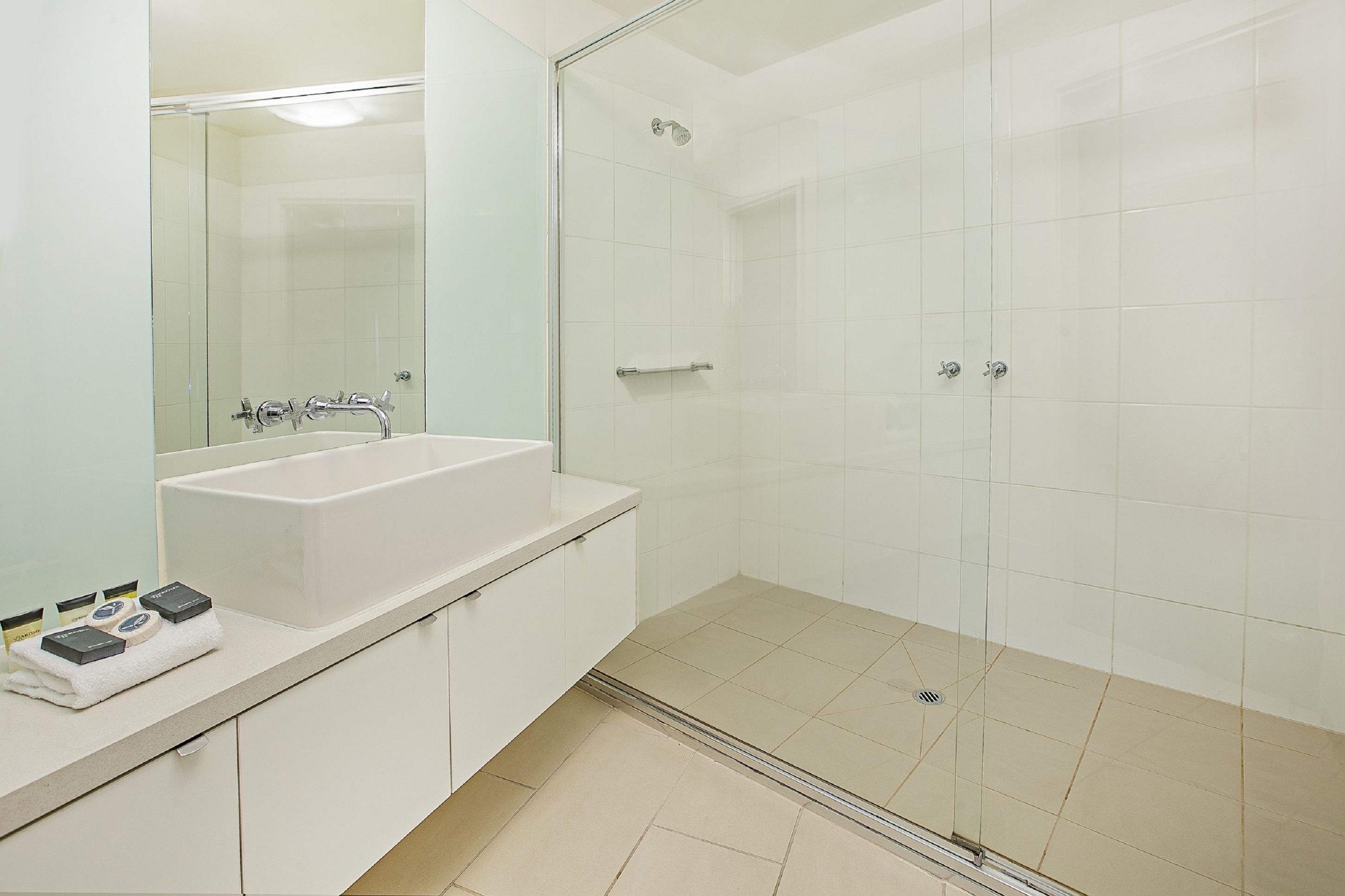 Un bagno moderno con un ampio lavandino bianco, cabina doccia in vetro e specchio sopra il lavandino.