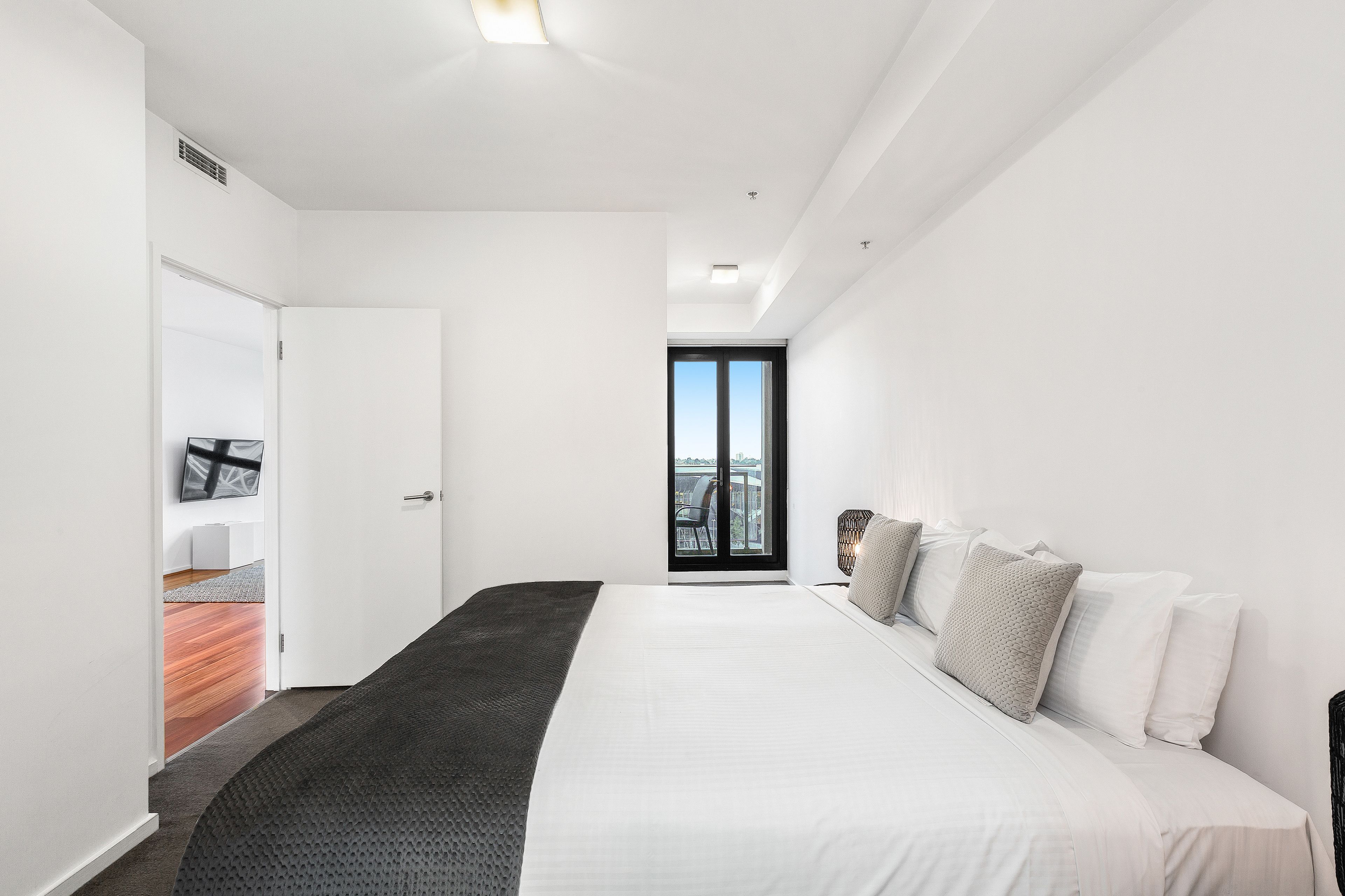 Un dormitorio moderno con una cama grande, vistas a través de un ventanal y una pequeña zona de estar con una silla y una mesa.