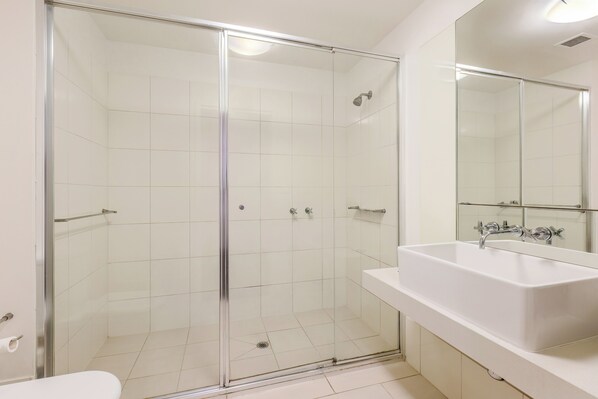 A modern bathroom with a glass-enclosed shower, a white sink, and a large mirror.