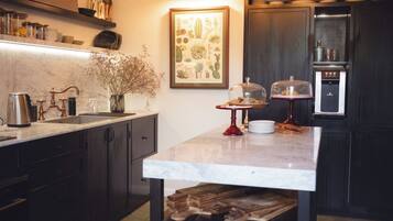 Una cocina con encimera de mármol, una araña, una mesa de madera con cuencos y un refrigerador.