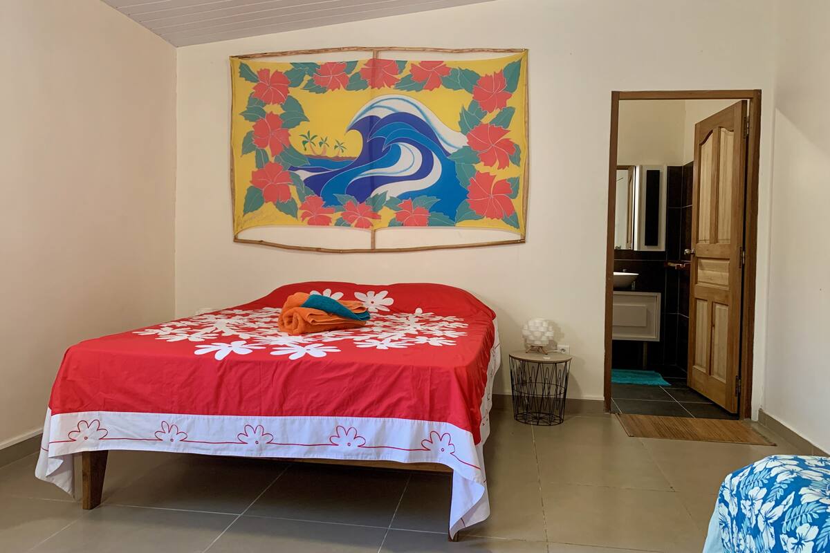A bedroom with a bed, a wall painting, a wooden door, and a bathroom visible through an open door.