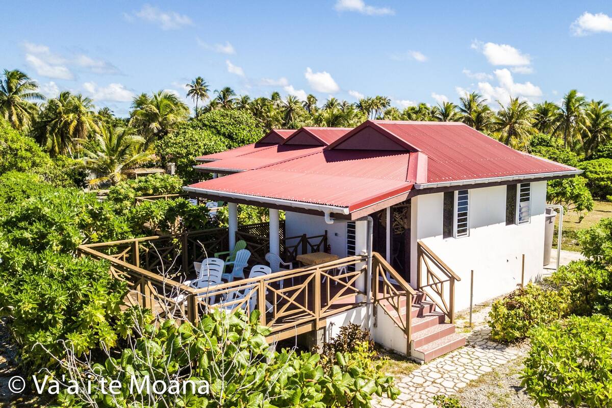 A small white building with a red roof, surrounded by lush greenery and palm trees.