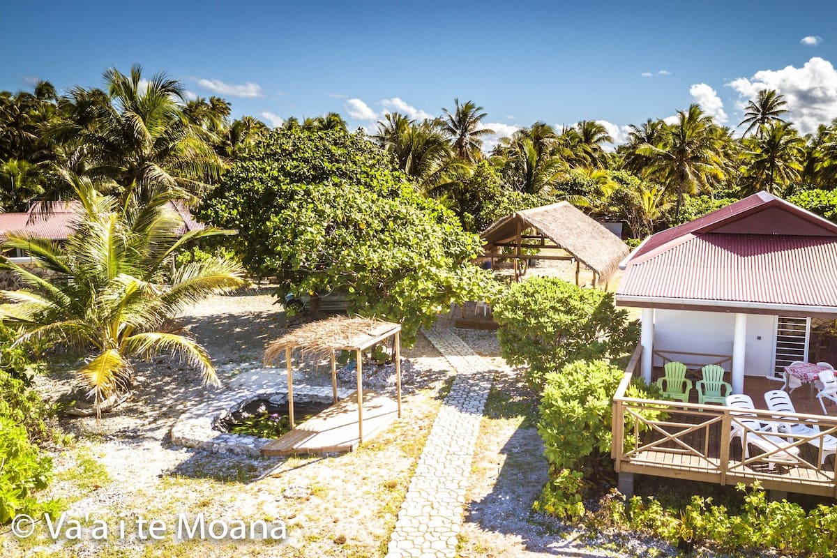 A bungalow with a thatched roof, a wooden deck with chairs, and a stone pathway.