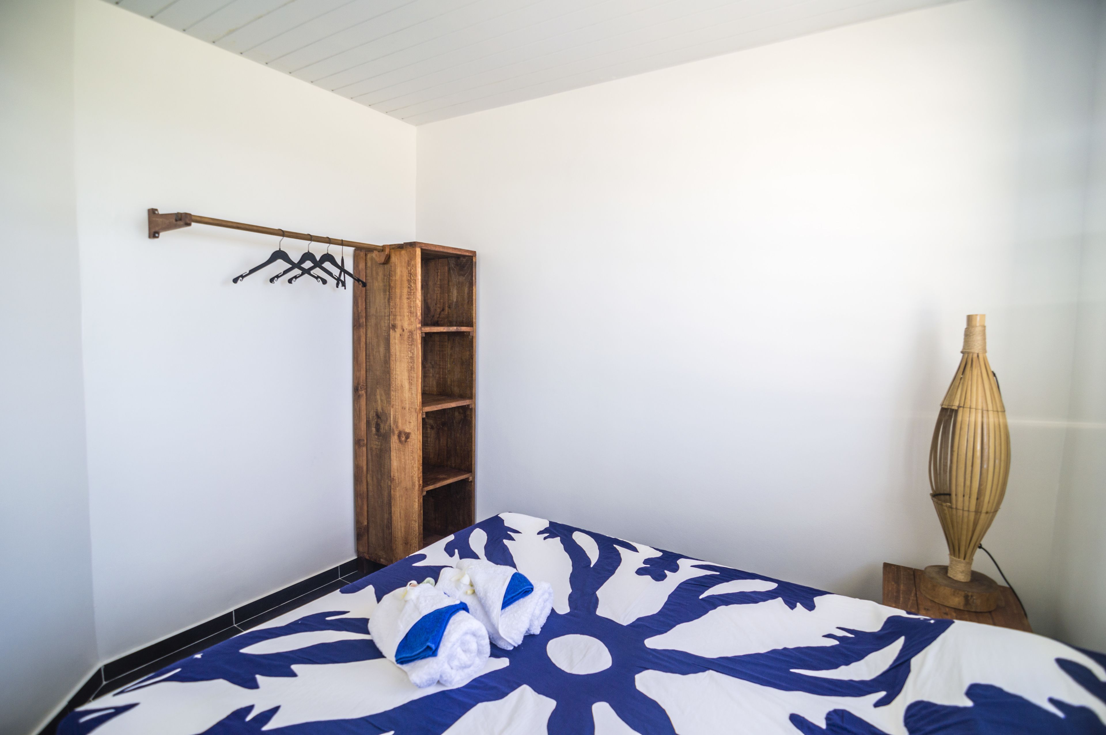 A bedroom with a bed, a wooden wardrobe, a towel rack, and a decorative lamp.