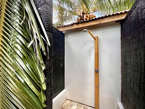 A small, enclosed shower area with a bamboo showerhead, surrounded by dark walls and a palm leaf. - Va'a i te Moana (Rangiroa)