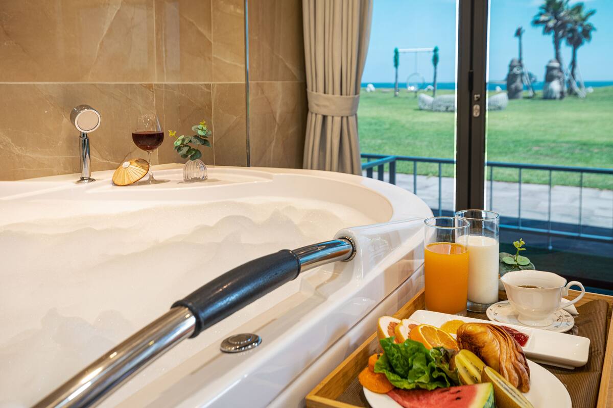 A bathroom with a bathtub, a towel rack, and a tray with breakfast items including toast, fruit, and a cup of coffee.