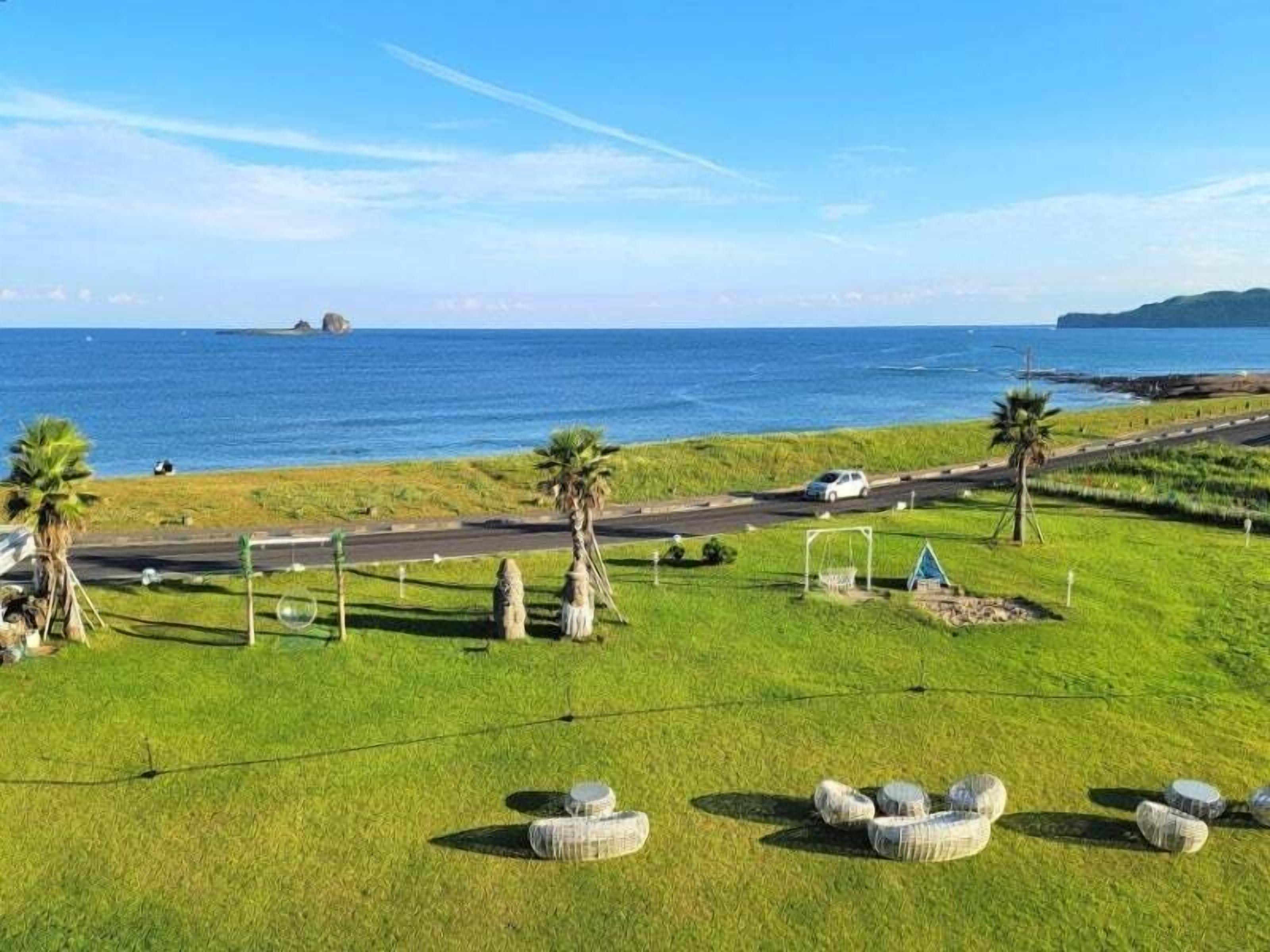 A coastal landscape with a road, grassy areas, and a few trees.