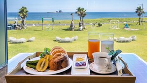 A breakfast tray with croissants, fruit, and beverages on a balcony overlooking a beach. - Sun & Moon Resort (Seogwipo)