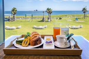 Bandeja de desayuno con cruasanes, fruta y bebidas en un balcón con vista a la playa.