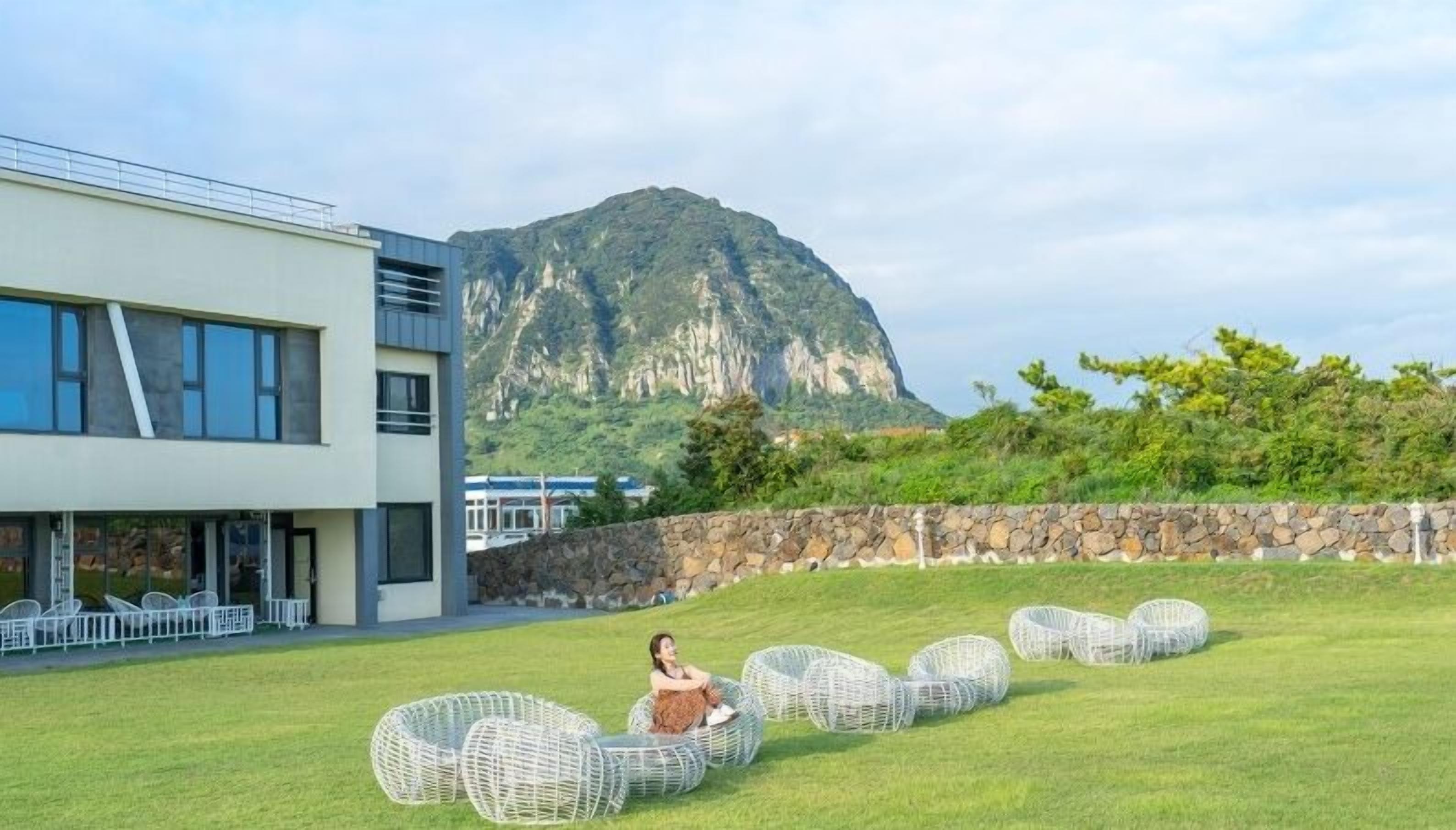 A modern building with a stone wall and a grassy area with wicker chairs.