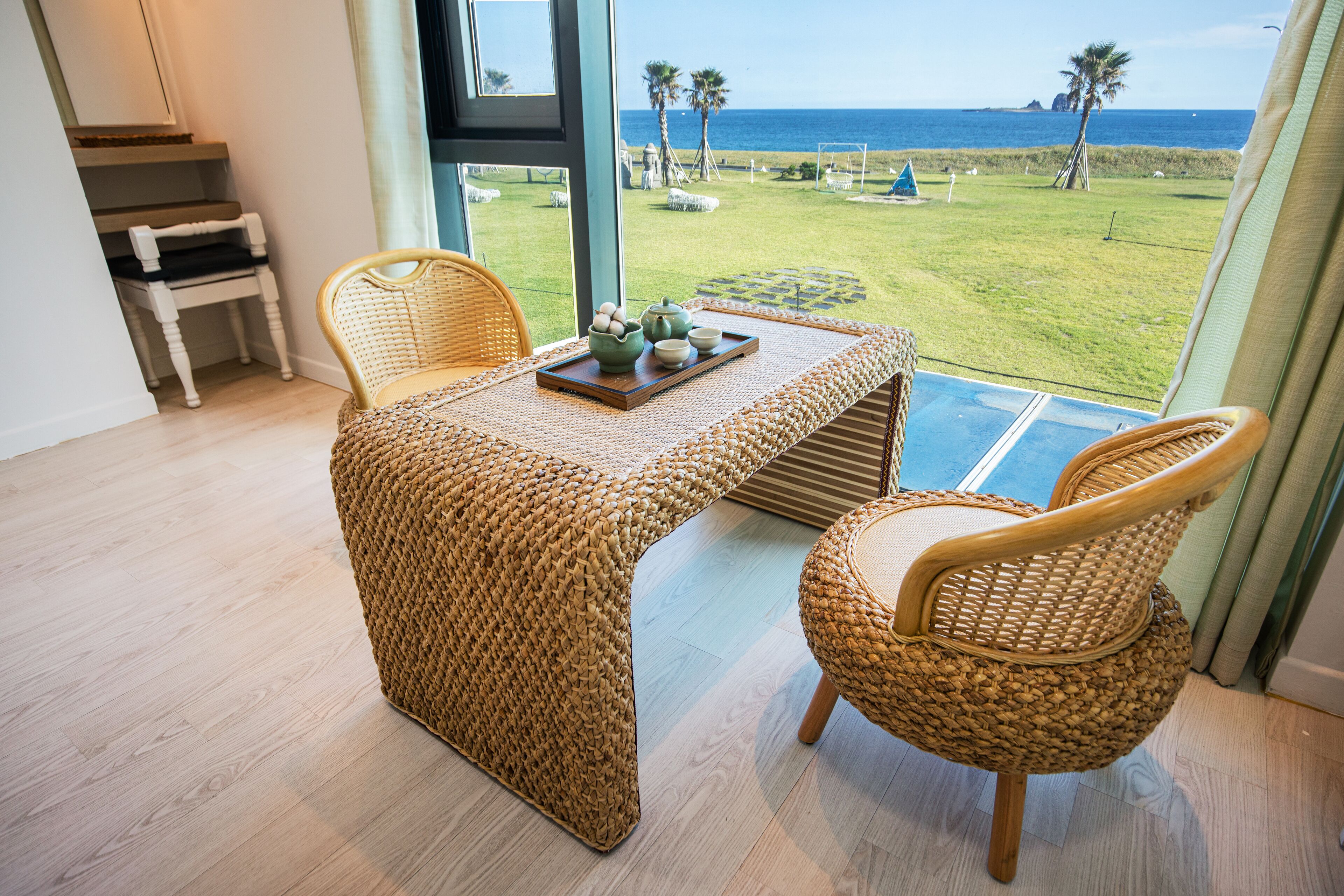 Un conjunto de comedor de mimbre con vista al océano y un área verde con palmeras.
