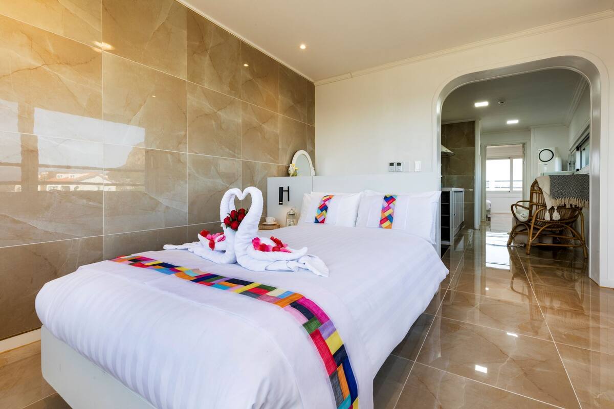 A hotel room with a large bed, a bathroom with a mirror and toiletries, and a dining area with chairs.
