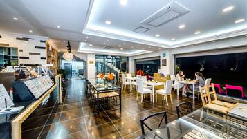 Un restaurant moderne doté d’un espace intérieur vaste et bien aménagé, d’un comptoir central où les plats sont servis et de différents types de sièges, notamment des tables et des chaises.