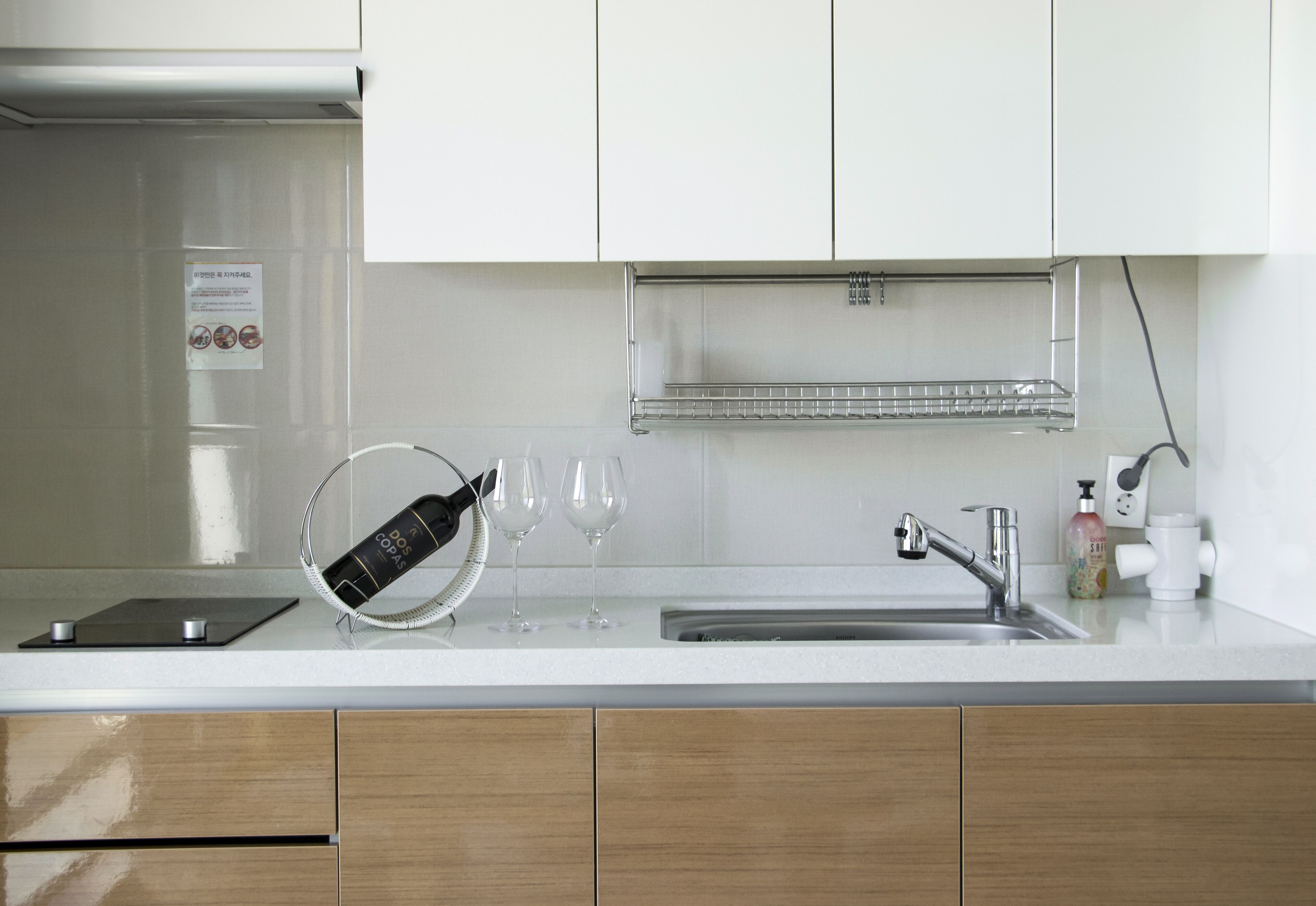 A modern kitchen with white cabinets, a stainless steel sink, a wine cooler, and a soap dispenser.
