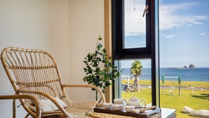 A wicker chair, a table with a tray of tea sets, and a view of the sea through a large window. - Sun & Moon Resort (Seogwipo)