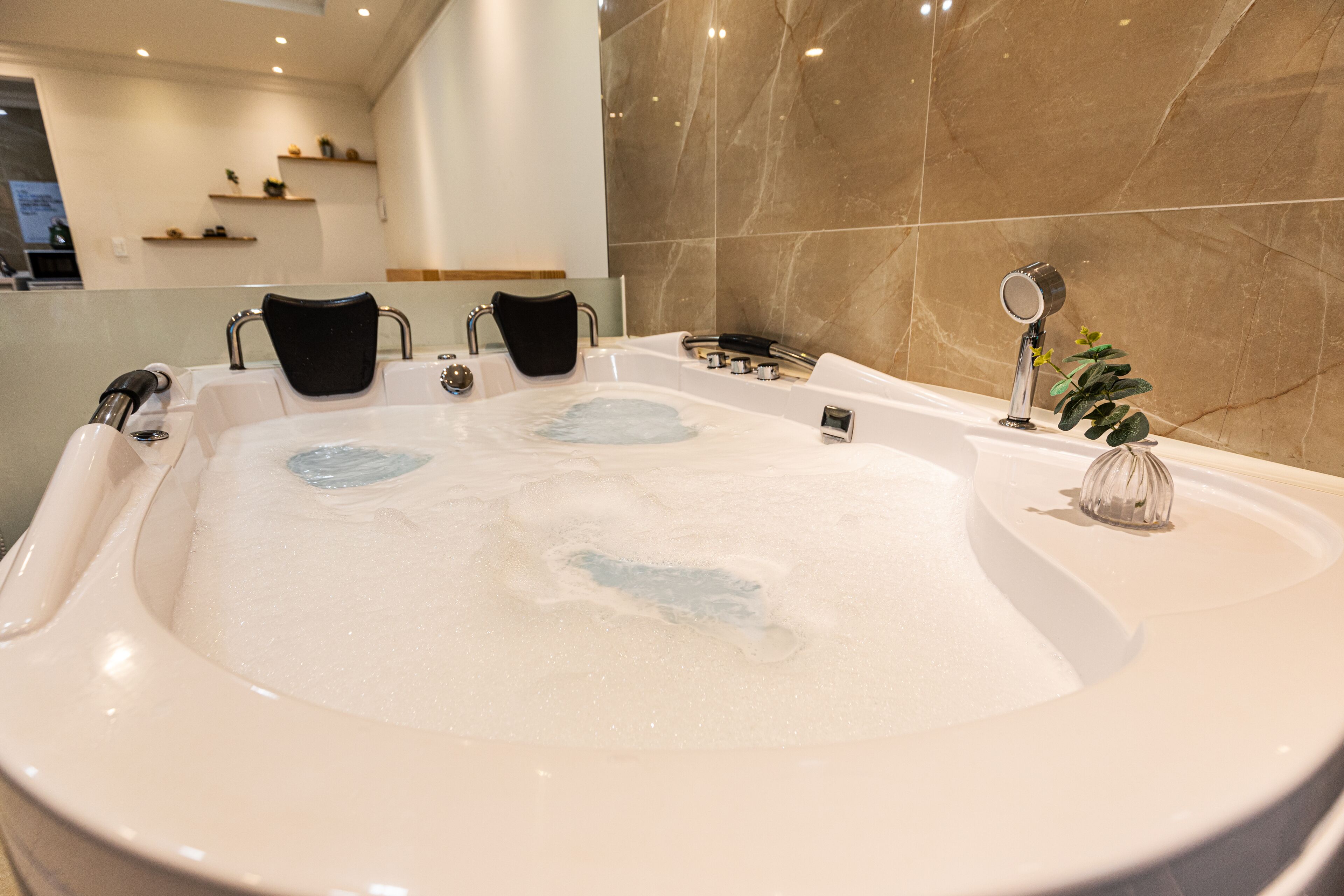 A large, modern bathtub with multiple jets, a small mirror, and a plant on the side.