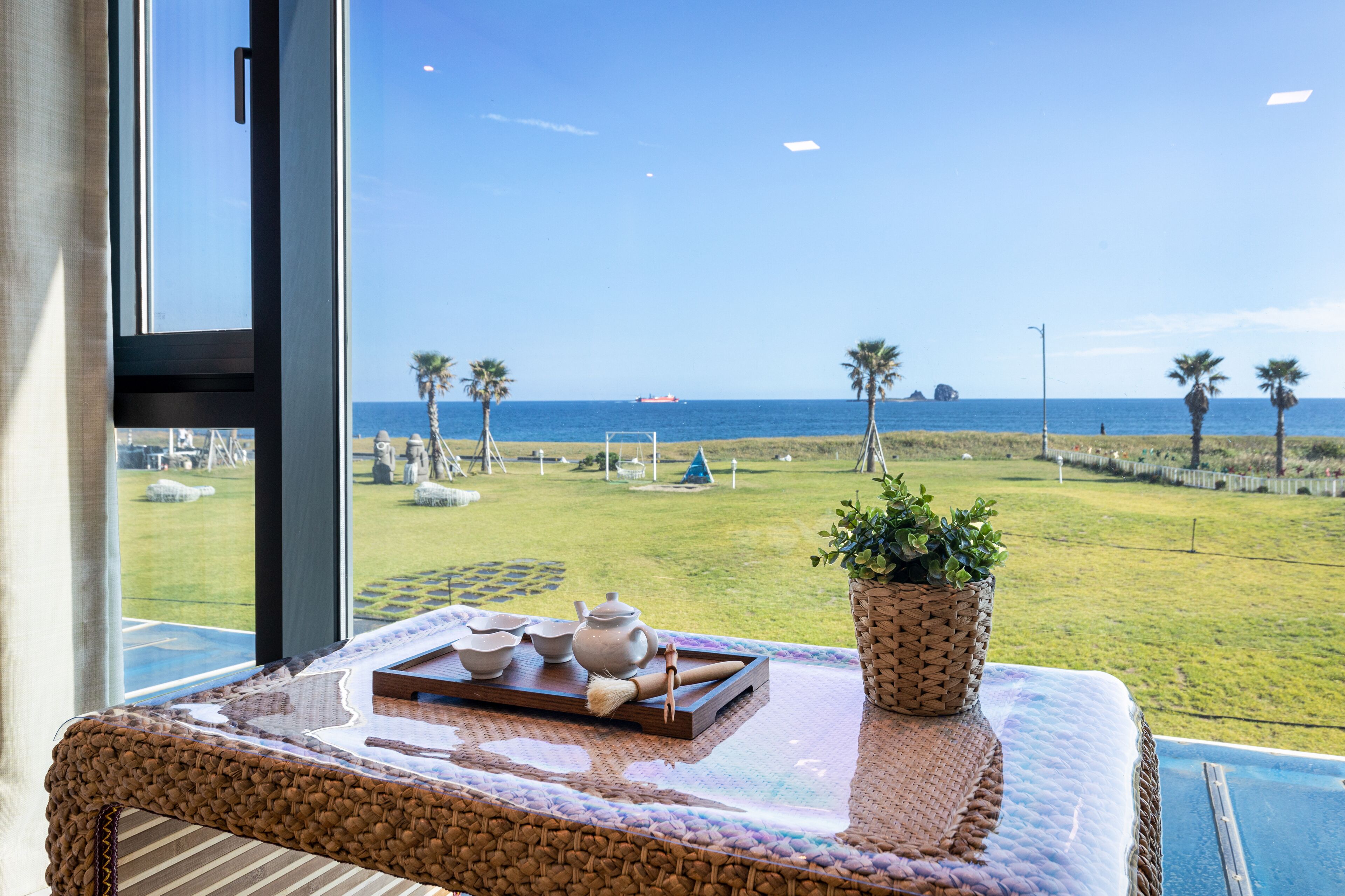 Vista desde un balcón con una mesa que muestra teteras y tazas, un mantel tejido y una planta en maceta.