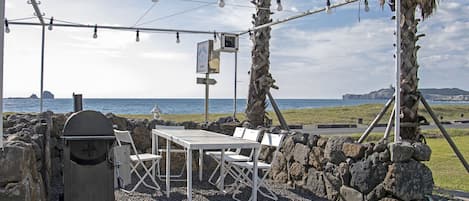 An outdoor seating area with a table and chairs, a grill, and string lights.