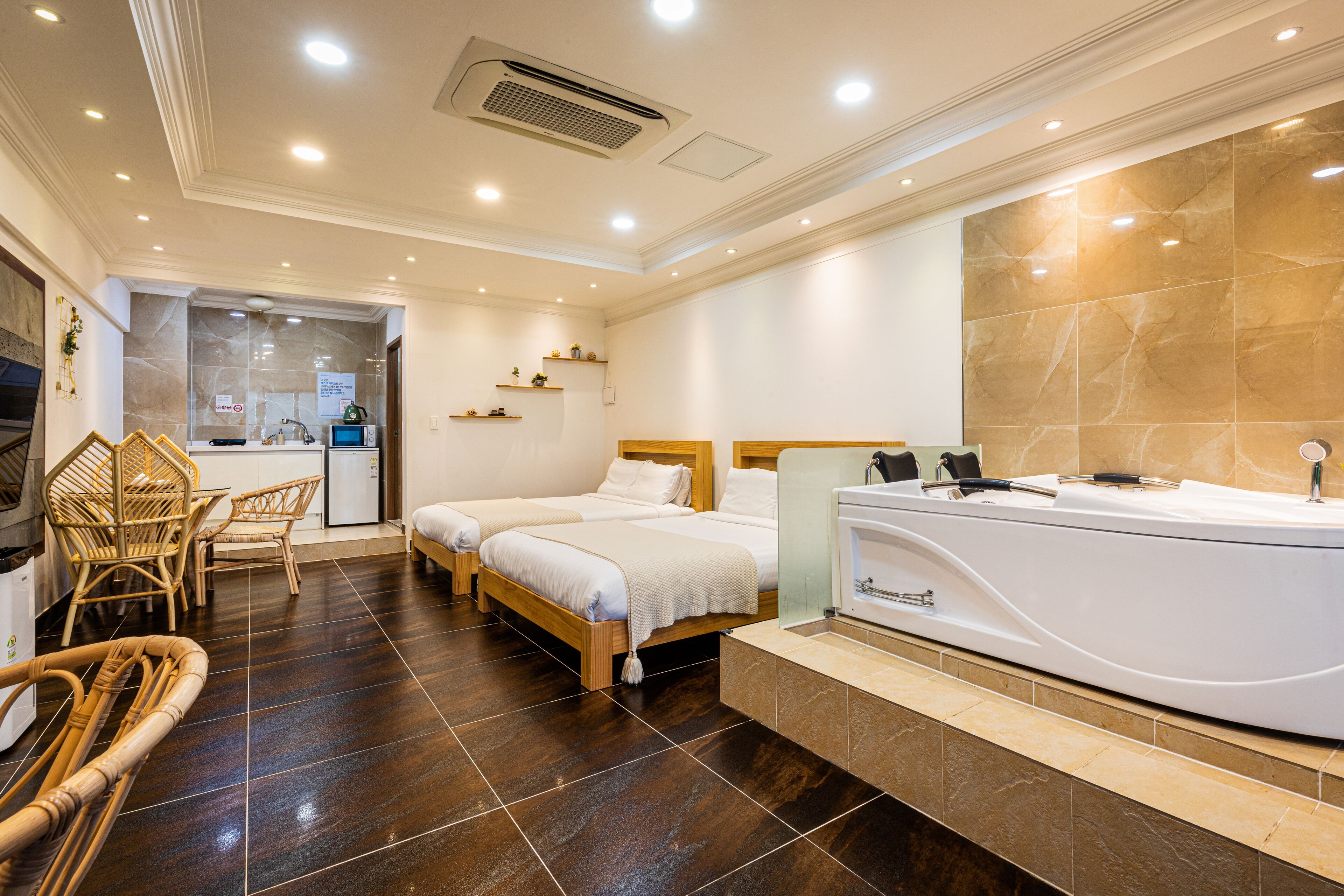 A hotel room with two beds, a bathtub, and a dining area with wicker furniture.