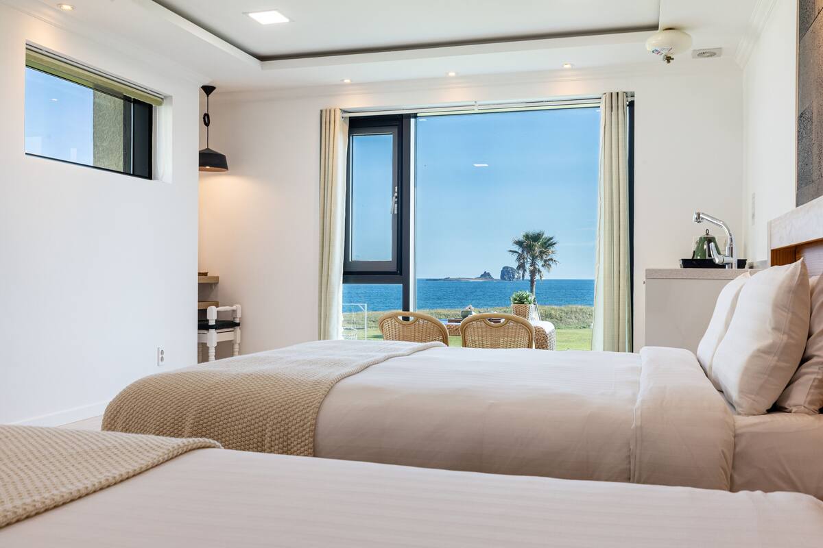 A hotel room with a large bed, a dining area with chairs, and a view of the sea.