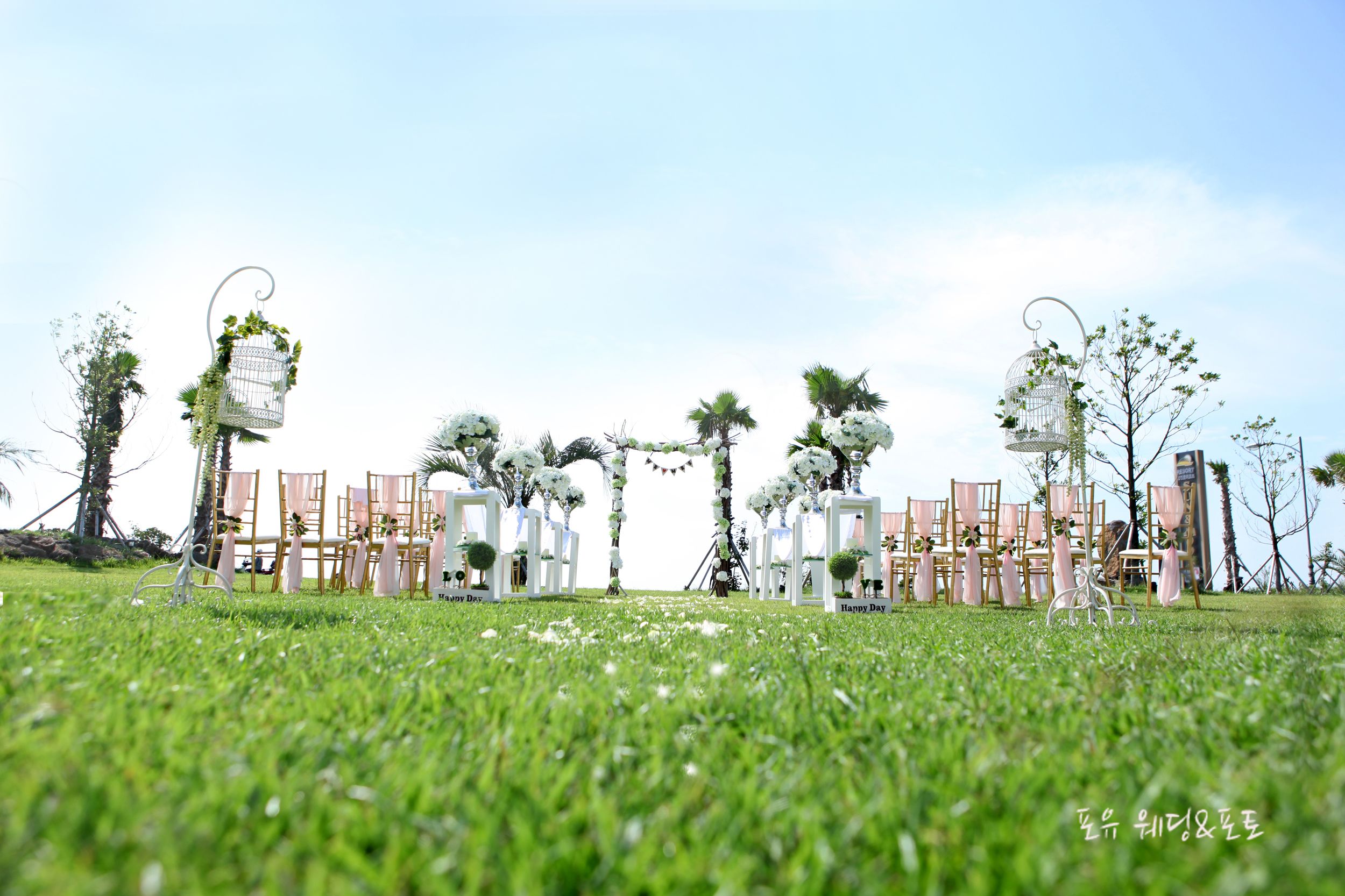 An outdoor wedding setup with white chairs, floral decorations, and hanging birdcages.